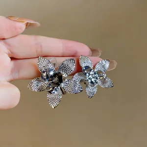 Dettaglio ravvicinato di orecchini a fiore con ago d'argento e finitura metallica