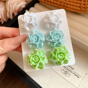 Close-up detail of three pairs of colorful resin rose stud earrings on a display card
