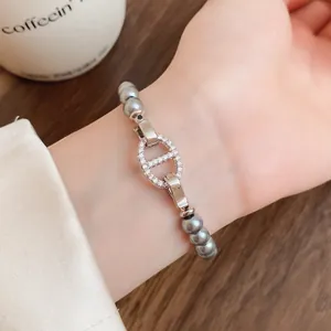 Nahaufnahme eines grauen Perlenarmbands mit einem glitzernden Glied am Handgelenk.