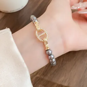 Detailaufnahme eines grauen Perlenarmbands mit glitzerndem goldenen Schweinenasen-Verschluss.