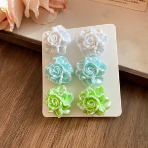 Detail view of pearlescent resin flower stud earrings set in white, blue, and green