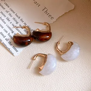Close-up detail of vintage C-shaped resin hoop earrings in brown and marble white