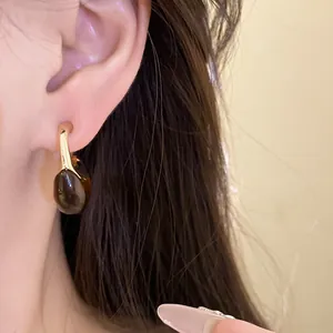 Close-up view of a resin C-shaped pendant earring worn on an ear with amber finish