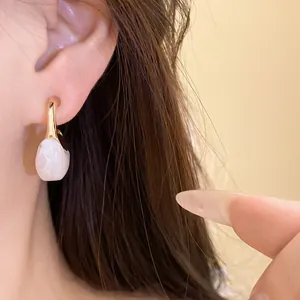 Close-up of elegant gold-tone C-shape earrings with a white marble resin teardrop pendant.