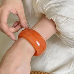Primer plano detallado de un brazalete ancho de acrílico veteado naranja en la muñeca