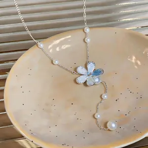 Detailed close-up of a delicate silver flower pendant and white pearl accents on the necklace