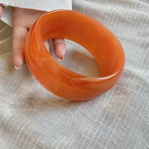 Detalle de un brazalete ancho de acrílico naranja veteado con estilo retro elegante.