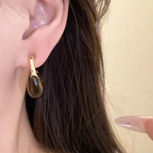 Close-up view of elegant brown resin drop earrings with gold finish worn on a female ear