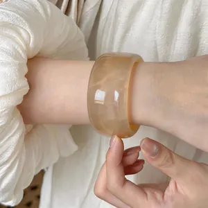 Detalle de un brazalete ancho de acrílico veteado ámbar en la muñeca, estilo retro vintage