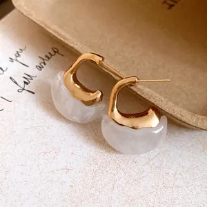 Detail view of gold and white marbled resin C-shaped earrings with retro design