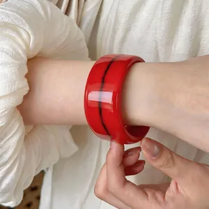 Primer plano de un brazalete ancho de acrílico rojo con veteado negro en la muñeca.
