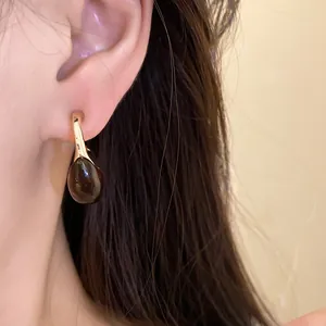 Detailed close-up of retro C-shape drop earring with dark amber resin pendant on ear