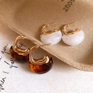 Close-up of vintage C-shaped resin earrings in amber and white marble style with gold.