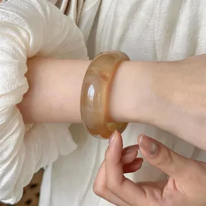 Detalle de cerca de un brazalete ancho de acrílico ámbar veteado en una muñeca femenina