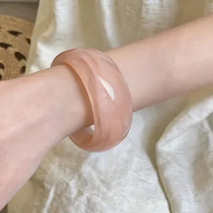 Vista de cerca de un brazalete ancho de acrílico jaspeado rosa en la muñeca