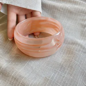 Primer plano de un brazalete ancho de acrílico marbreado con espirales rosa retro