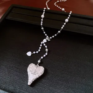 Detailed macro view of elegant pearl beaded necklace with ornate heart pendant on black tray.