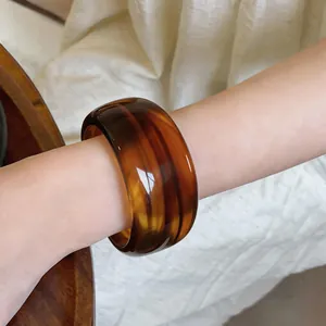 Detalle de un brazalete ancho de acrílico ámbar con patrón de carey en la muñeca
