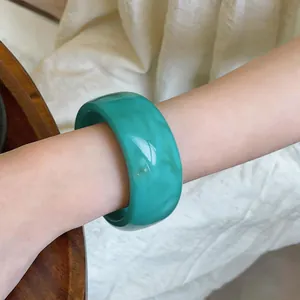 Primer plano detallado de un brazalete ancho de acrílico marbreado verde en la muñeca.
