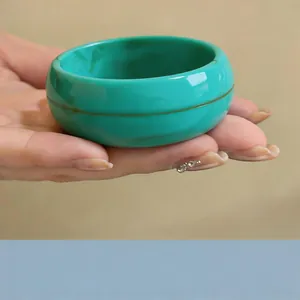 Primer plano de un brazalete redondo ancho de acrílico jaspeado verde azulado en la mano
