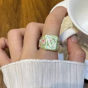 Close-up of a chunky green enamel ring with delicate floral patterns and pearl details.