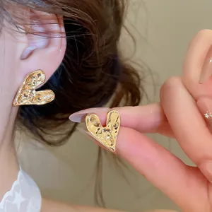 Close-up of textured gold heart stud earrings showing unique irregular wrinkled finish