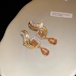 Primo piano di orecchini a goccia in oro con zirconi champagne e dettagli a forma d'ali
