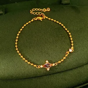 Elegant gold ball chain bracelet with purple kite-shaped zirconia on green velvet