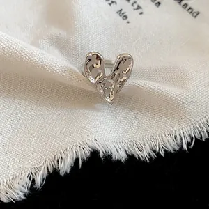 Close-up of a silver wrinkled heart ring on a cream textured fabric background