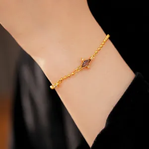 Elegant gold bracelet featuring a purple rhombus zircon, displayed on a delicate wrist.