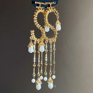 Dettaglio di orecchini a lettera S placcati oro con nappe di perle e finiture eleganti.