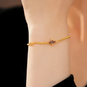 Close-up detail of an elegant gold bead bracelet featuring a purple rhombic zircon on a wrist