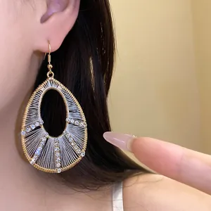 Close-up of gold teardrop earrings with silver thread and rhinestones worn by model