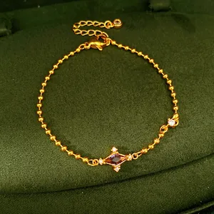Close-up of elegant gold ball chain bracelet with purple rhombus zircon on green velvet.