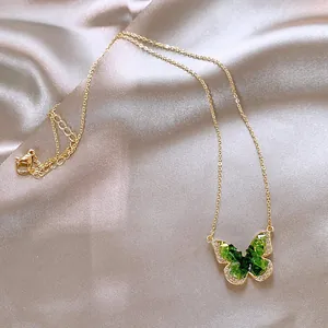 Close-up detail of a green gradient butterfly pendant on a gold-tone necklace chain