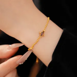 Close-up of elegant gold bead bracelet with a rhombic purple zircon center stone