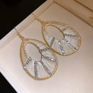 Close-up of elegant gold-toned teardrop earrings with woven thread and crystal detail
