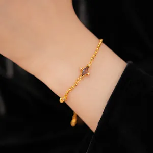 Close-up of a gold beaded bracelet featuring a purple rhomboid zircon centerpiece.