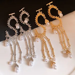 Dettaglio di orecchini metallici a forma di S con eleganti nappe di perle bianche