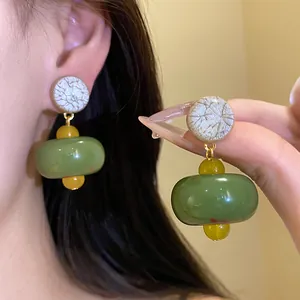 Detailed macro view of elegant green resin drop earrings featuring textured cream discs
