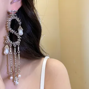 Primo piano di eleganti orecchini a goccia in metallo a forma di S con nappe di perle