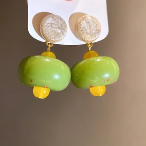 Macro view showing the detail of green and yellow resin pendant earrings with textured studs