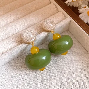 Close-up of olive green and cream resin drop earrings with silver needle in jewelry tray