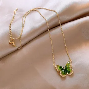 Detailed close-up of an elegant gold butterfly pendant necklace with green gradient crystals