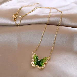 Detailed view of a gold-plated necklace with a green gradient butterfly pendant on satin