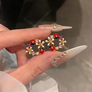 Primo piano di orecchini a corona con coccinella e fiori placcati oro 18k con zirconi.