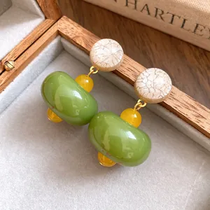Close-up of green resin drop earrings with marble-textured studs and yellow beads.