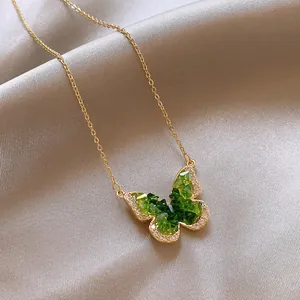 Detailed macro shot of a gold butterfly pendant necklace inlaid with green crystals.