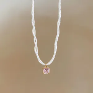 Close-up detail of a twisted white pearl necklace featuring a square pink gemstone pendant