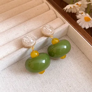 Close-up of green resin drop earrings with textured beige top and yellow bead